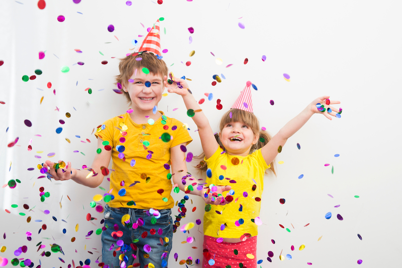 happy two kids brother and sister with confetti on colored yellow background